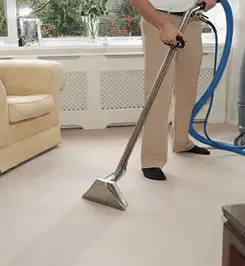 Professional carpet cleaner using a hot-water extraction wand and hose machine in a living room in Dayton, OH.