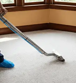 Steam carpet cleaning technician using a hot-water extraction wand on a residential carpet, wearing blue protective shoe covers Dayton, OH.