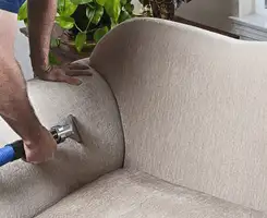 Professional upholstery cleaner deep-cleaning a fabric sofa with a handheld extraction tool and hose in Dayton, OH.